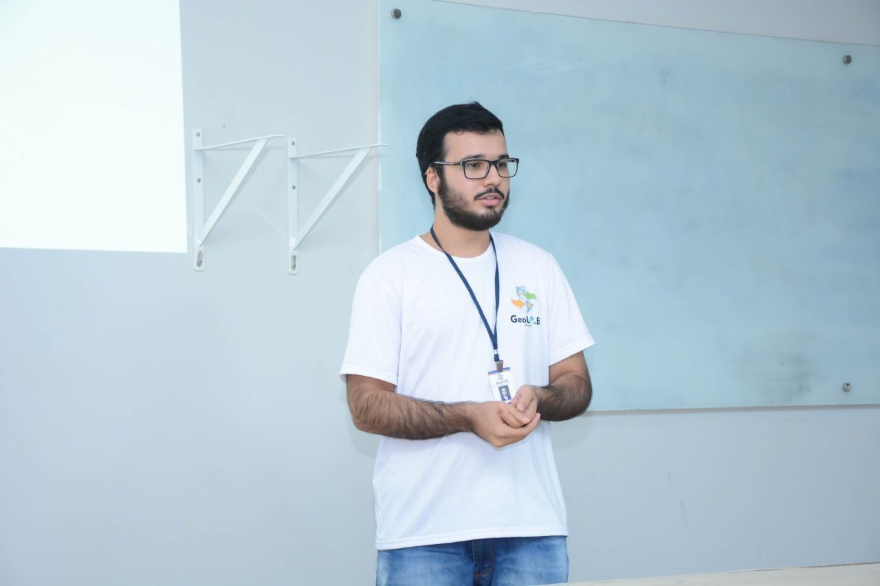 Um homem usando óculos e um cordão está parado em frente a um quadro branco.