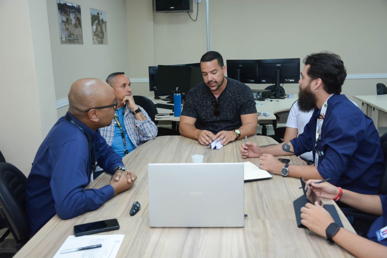 Um grupo de pessoas está sentado ao redor de uma mesa com um laptop sobre ela
