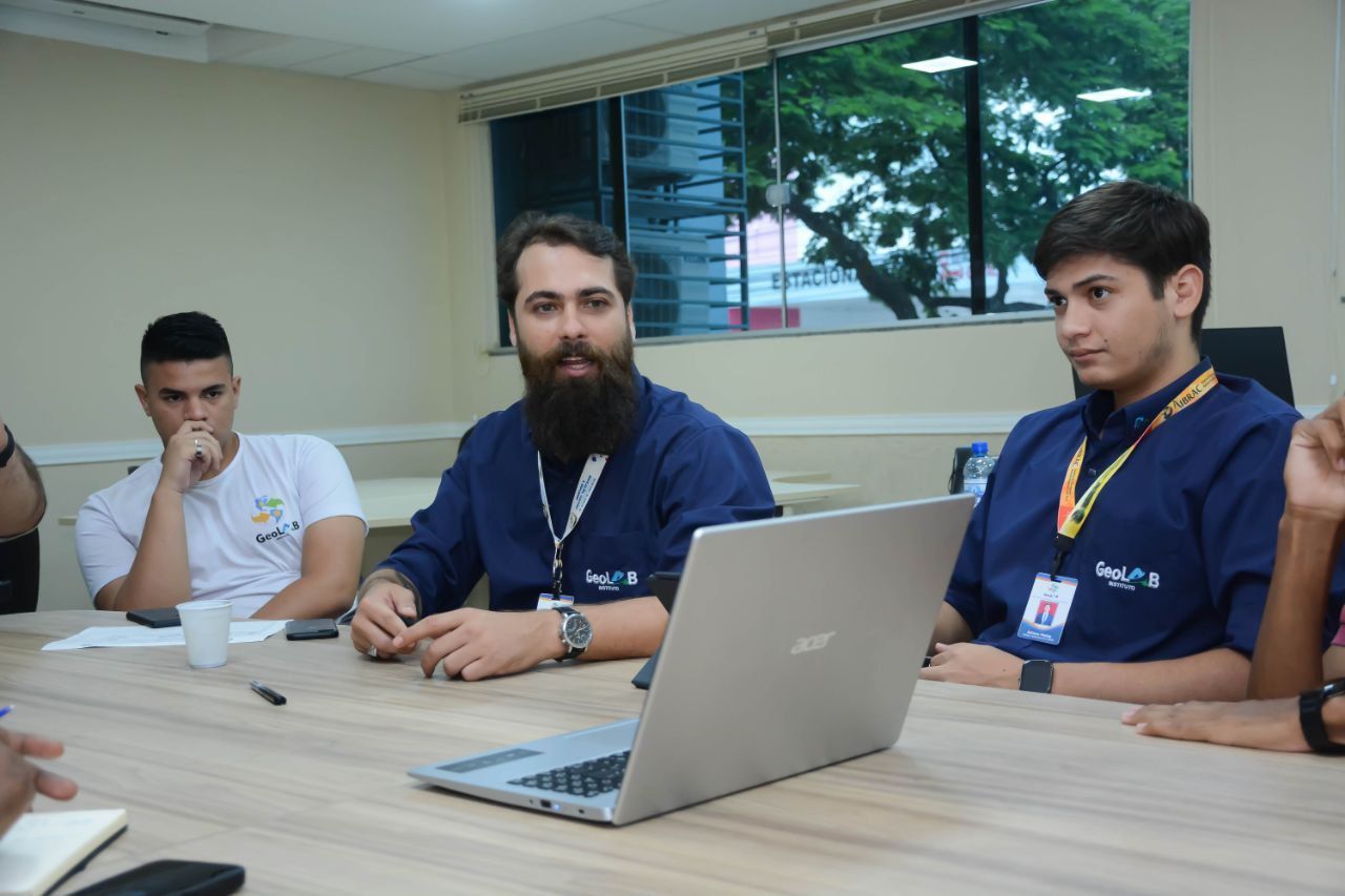 Um grupo de homens está sentado em uma mesa com um laptop sobre ela.