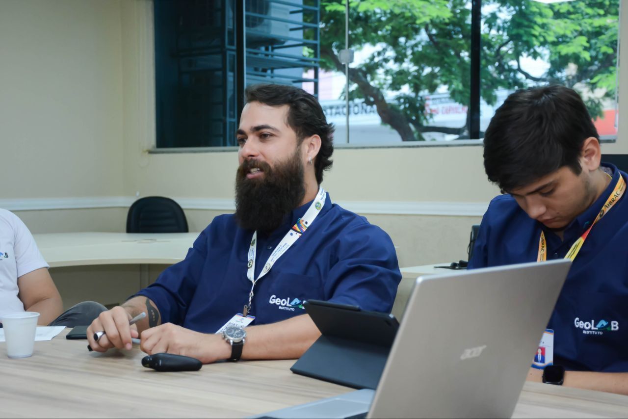 Um homem com barba está sentado em uma mesa com um laptop.