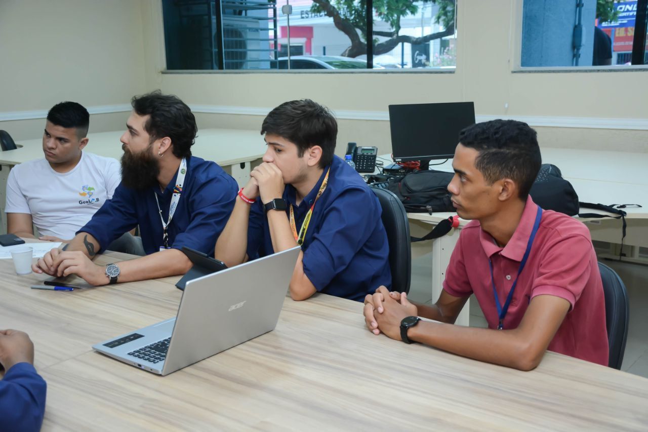 Um grupo de homens está sentado em uma mesa com laptops.