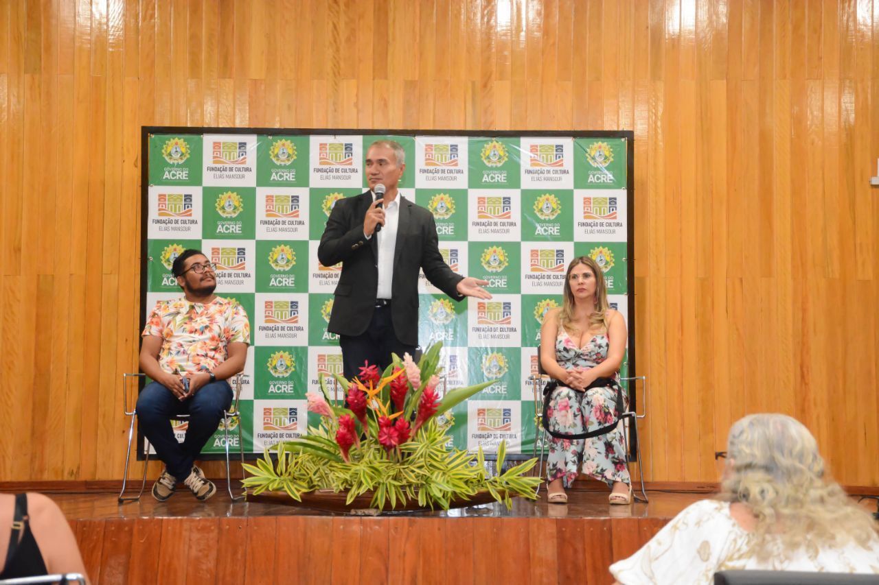 Um homem está em pé no palco segurando um microfone na frente de um grupo de pessoas.