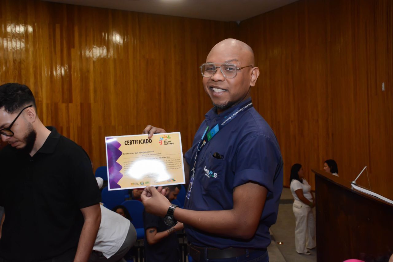 Um homem de camisa azul está segurando um certificado em uma sala.