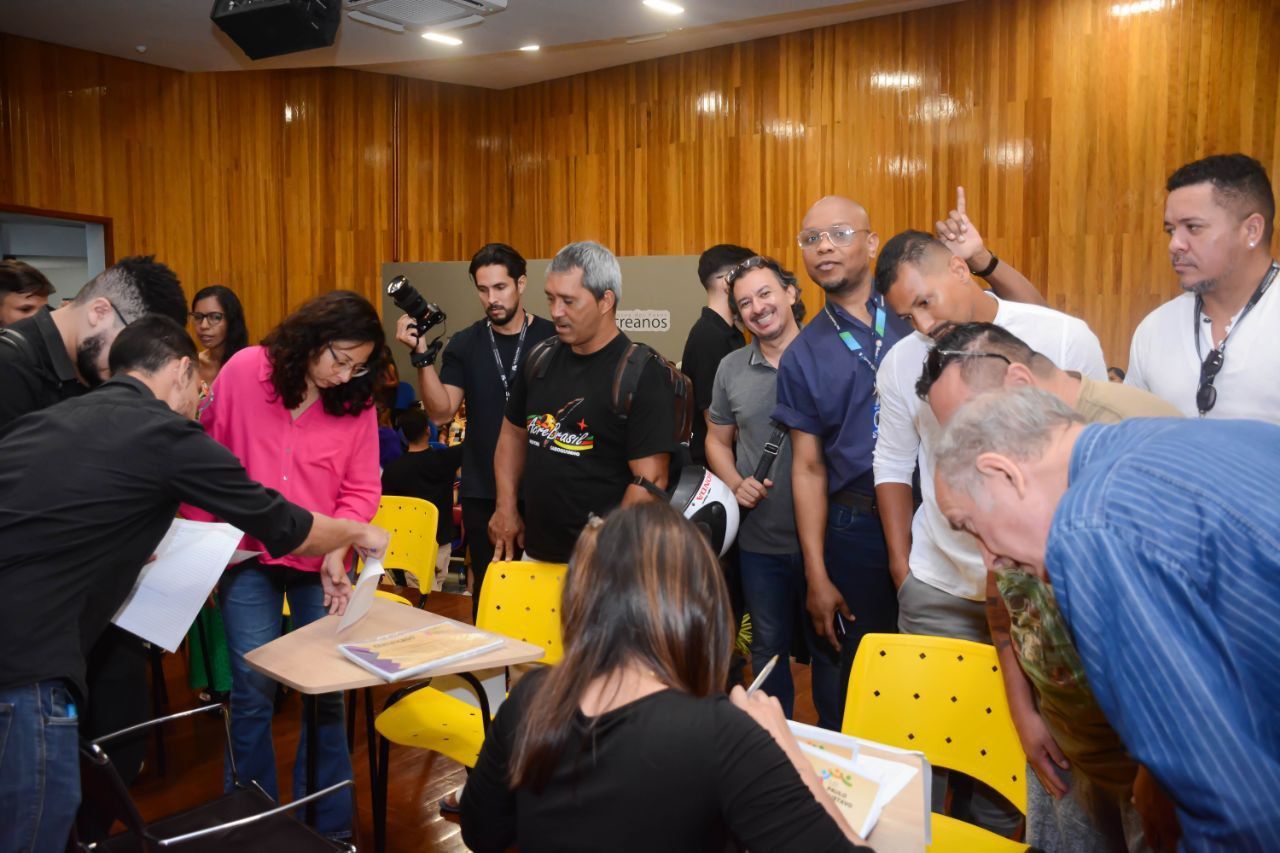 Um grupo de pessoas está em volta de uma mulher em uma sala de aula.