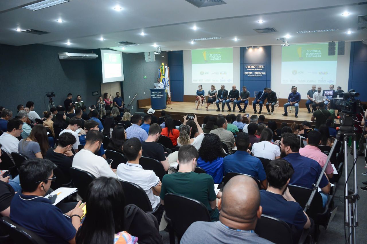 Um grande grupo de pessoas está sentado em um auditório assistindo a uma apresentação.