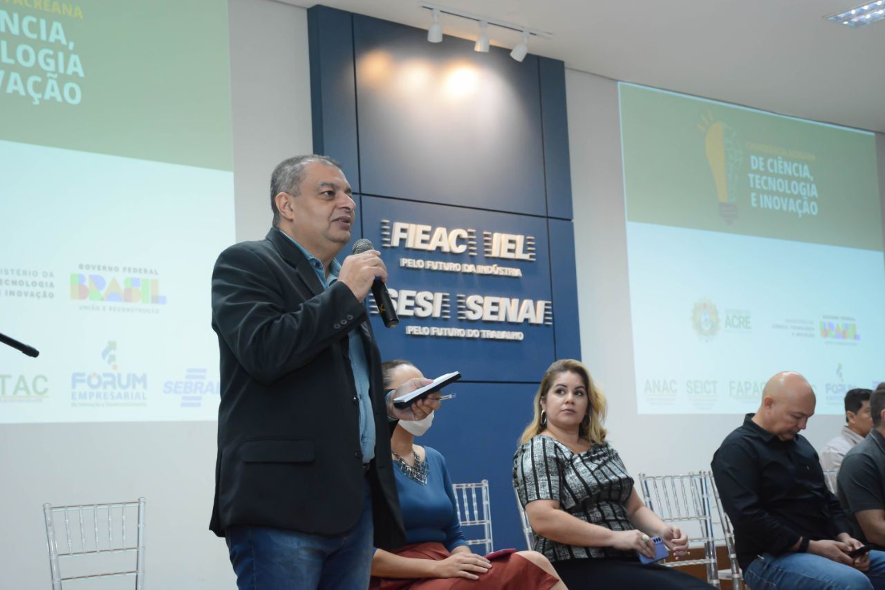 Um homem está falando em um microfone na frente de um grupo de pessoas