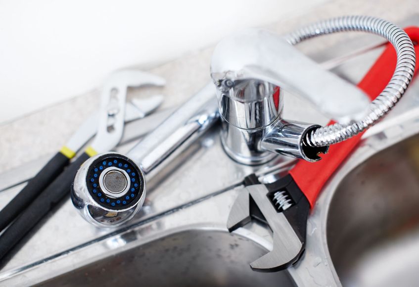 A wrench is sitting on top of a sink next to a faucet.