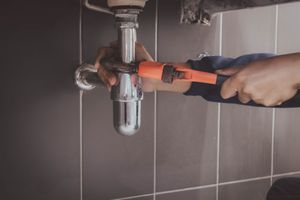 A plumber is fixing a sink pipe with a wrench.