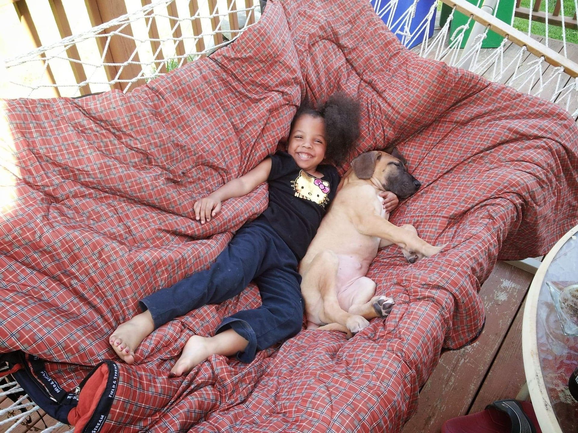 Child and puppy lounging on a red patterned couch, both lying on their sides and looking relaxed