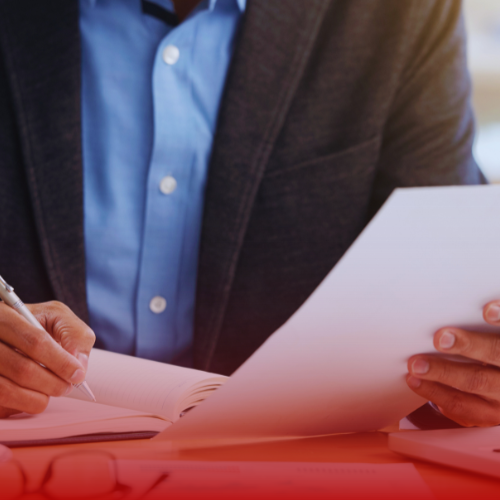 A man writing something in a notebook while holding a paper