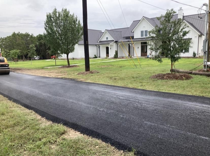 A man spreads blacktop asphalt sealant evenly on a residential driveway using a large brush.