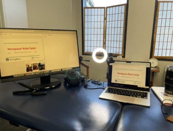 Desktop, laptop and microphone on top of a physical therapy table.