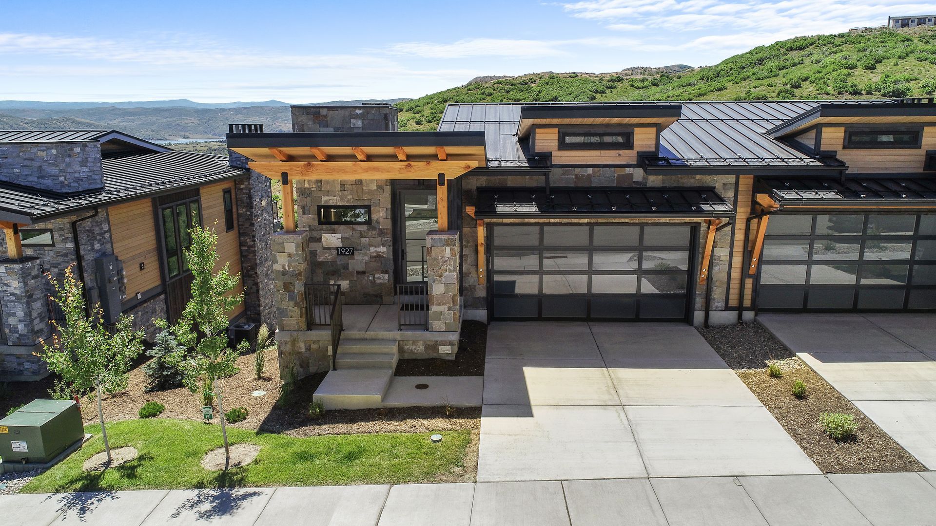 Modern home with stone and wood exterior, glass garage doors, and mountain view.