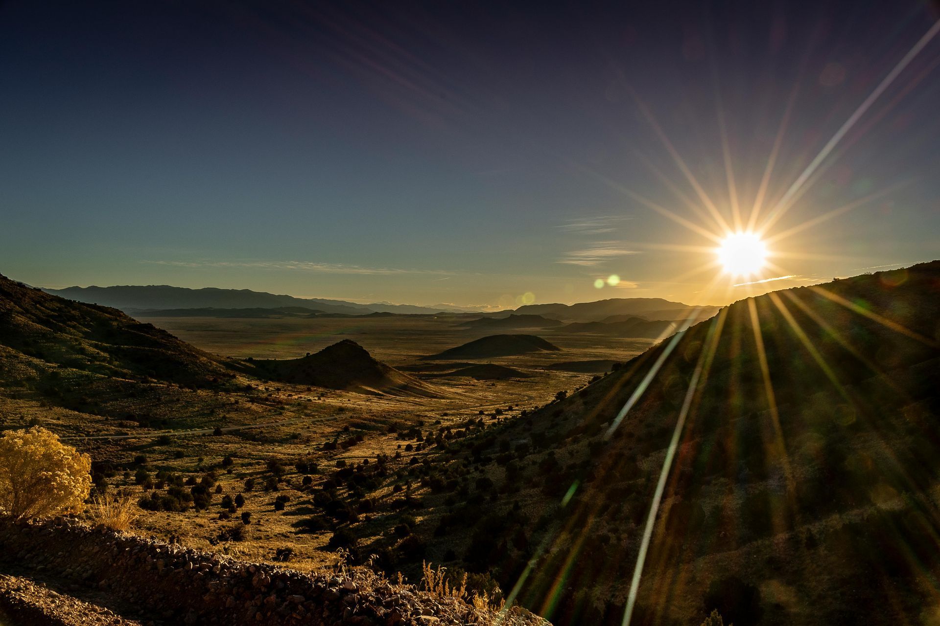 Sunrise over a valley and mountains; lens flare creates bright rays.
