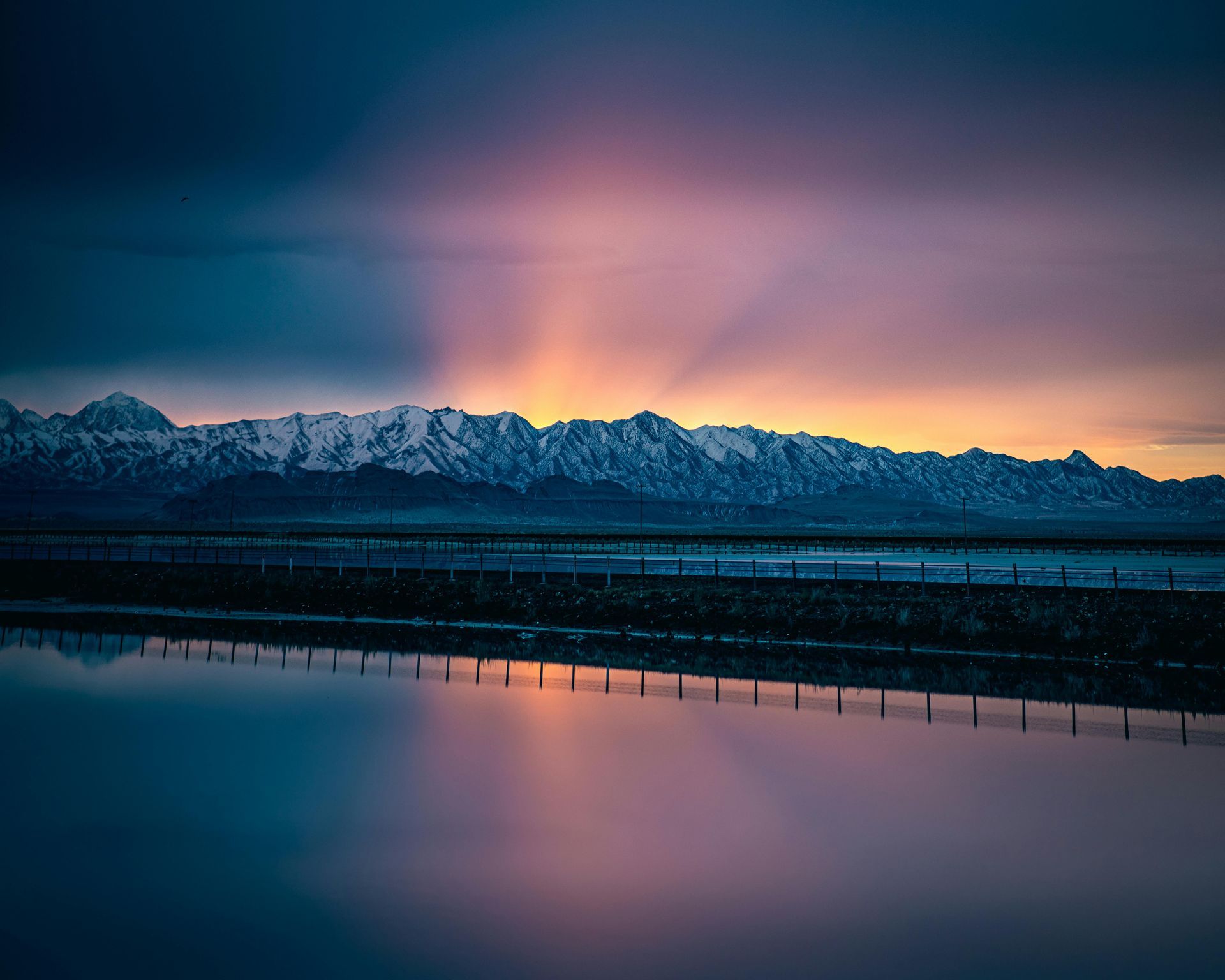 Snow-capped mountains reflected in still water under a colorful, dramatic sunset.