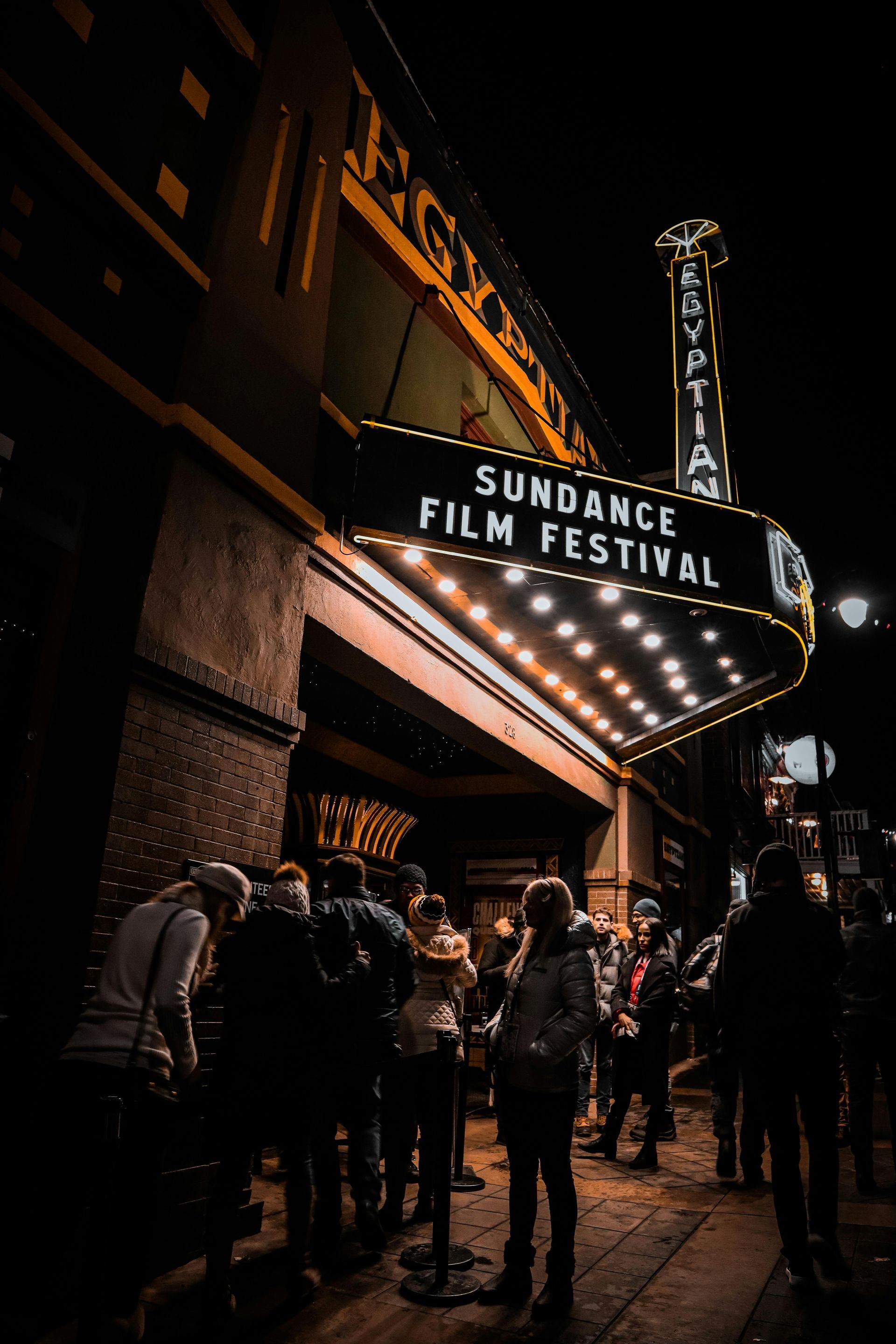 The Egyptian Theatre at night: Sundance Film Festival marquee illuminated, people in line, dark setting.