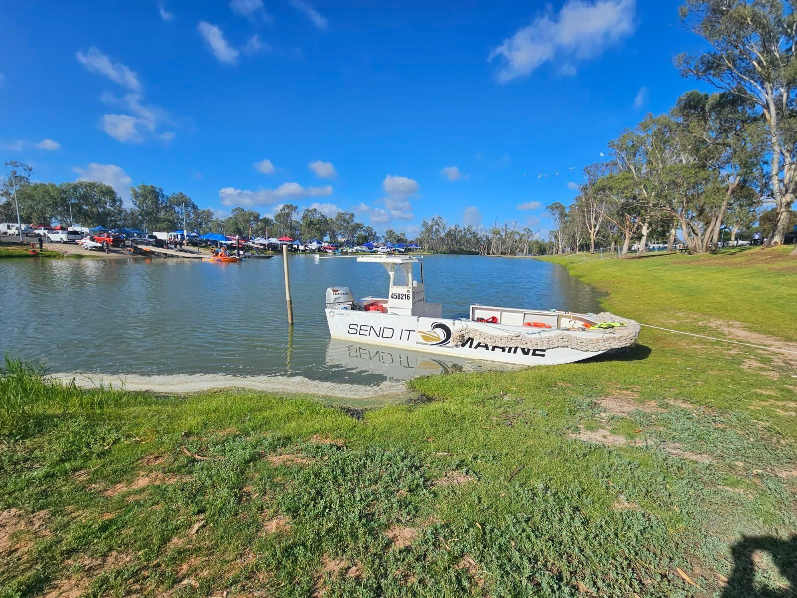 a white boat is on a trailer next to a body of water .