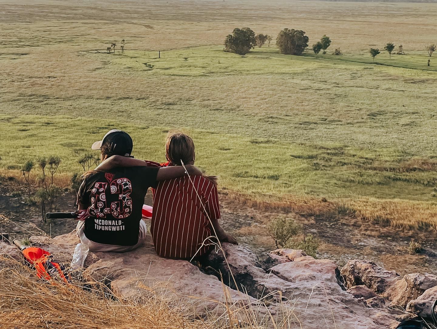 A man and a woman are sitting on a rock overlooking a field.