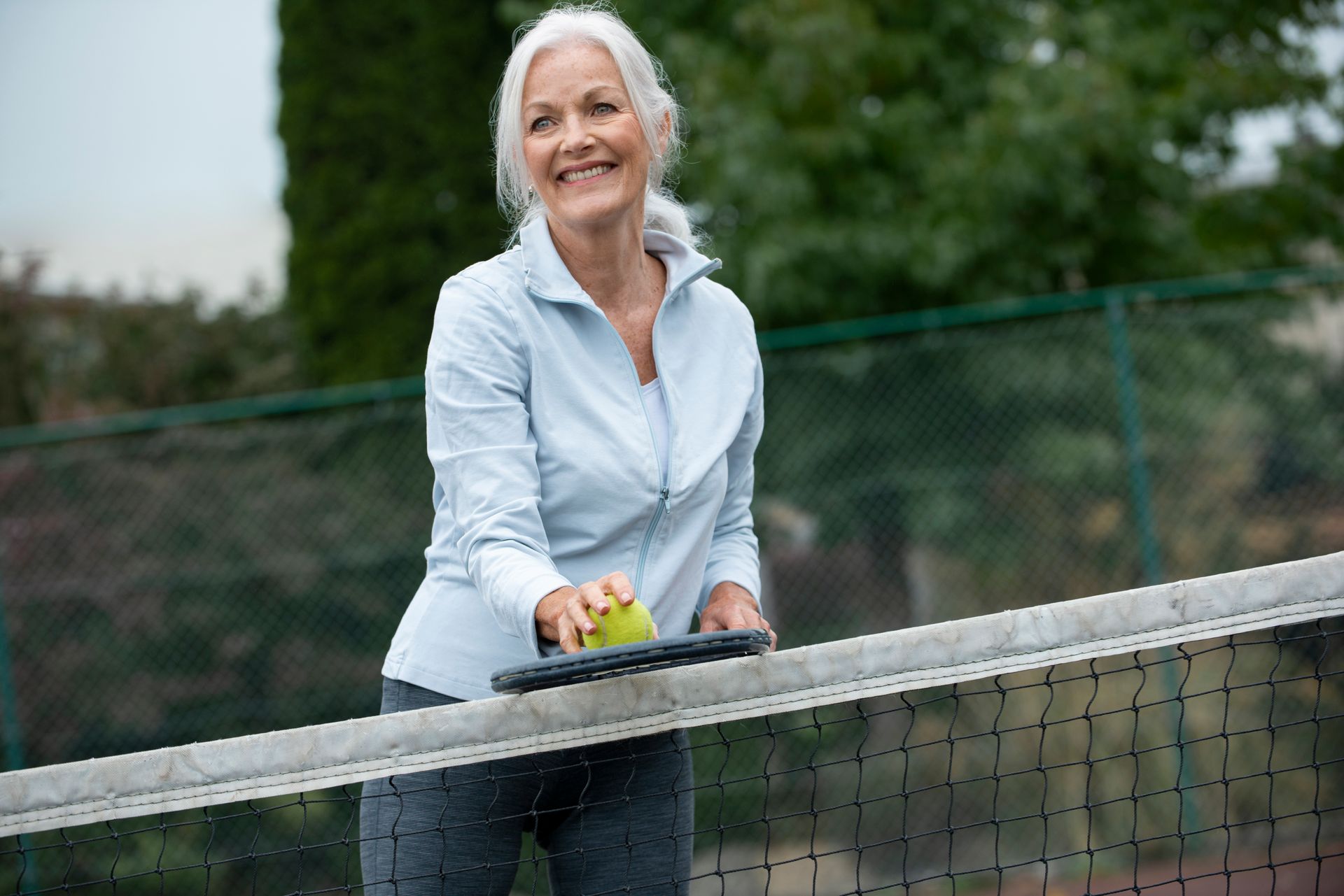 An older woman is playing tennis on a tennis court.