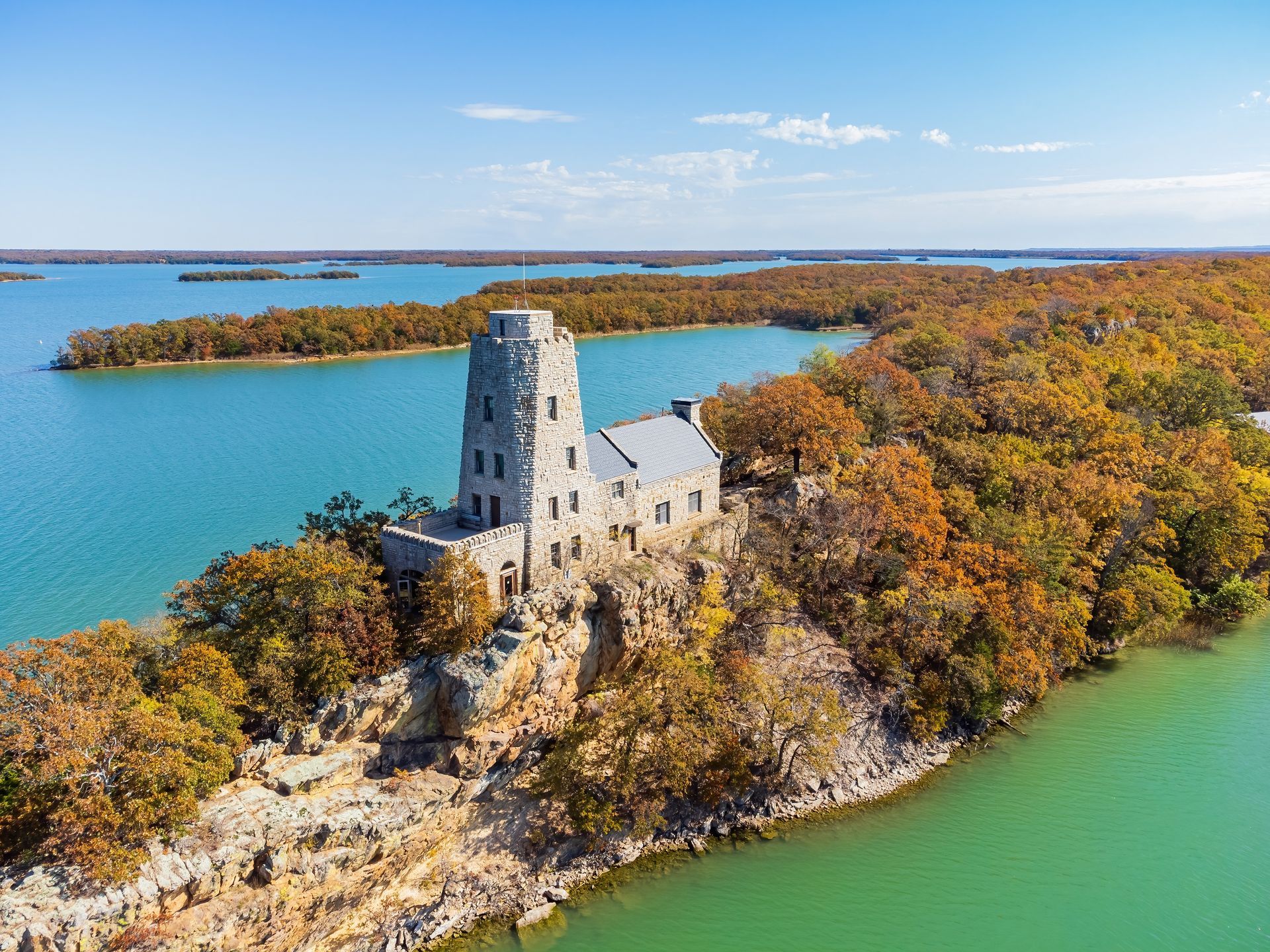 An aerial view of a castle on top of a small island in the middle of a lake surrounded by trees.