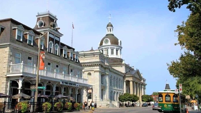 A green trolley is driving down a street in front of a large building.