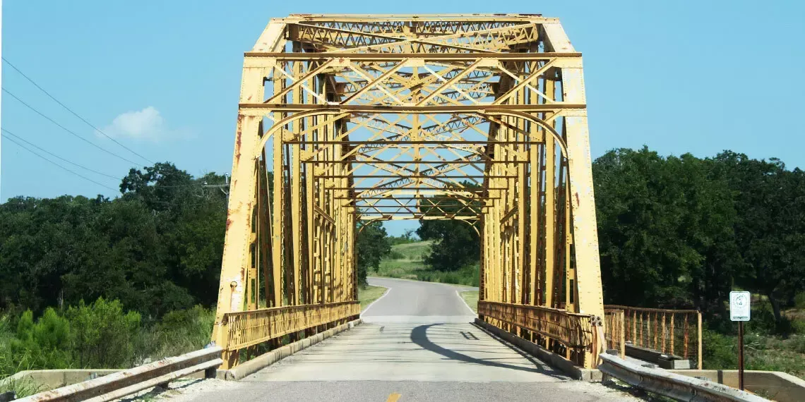 A yellow bridge over a road with trees in the background