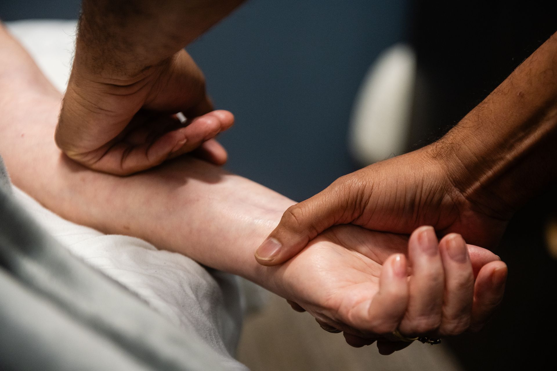 Person manipulating another person's arm. Light-skinned arm held by person in gray sweater, likely for therapy.