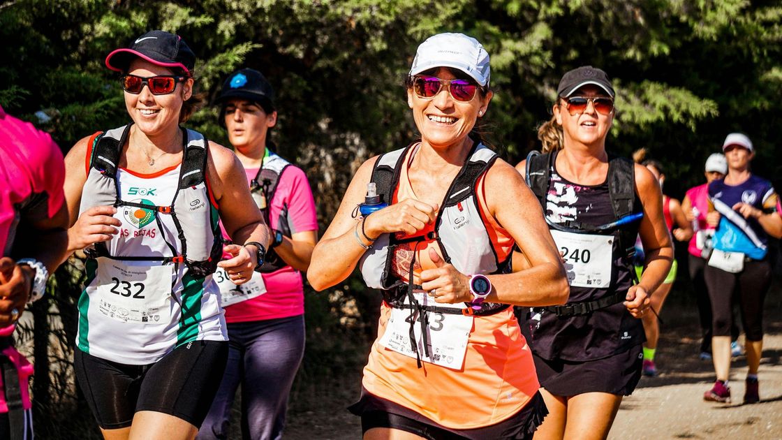 Runners in hats and hydration packs on a trail; sunny day, smiles, thumbs up.