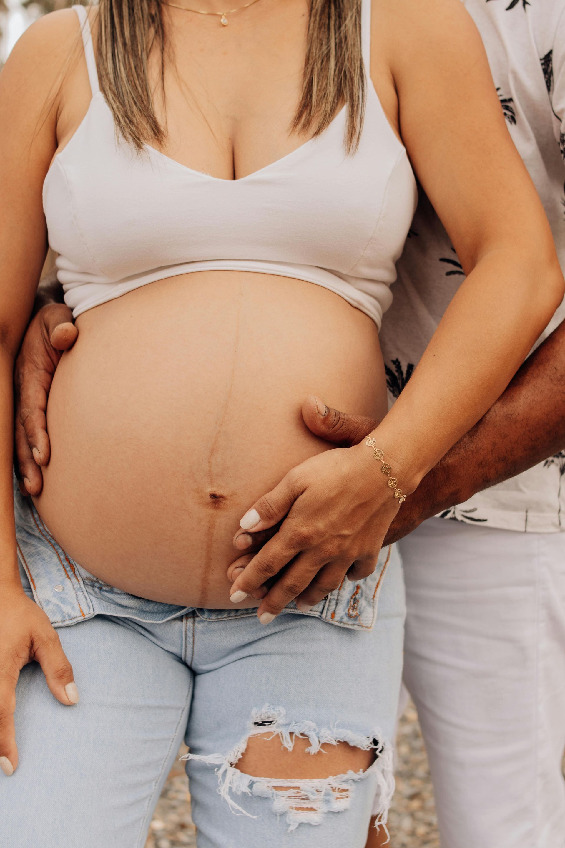 A pregnant woman is standing next to a man who is holding her belly.