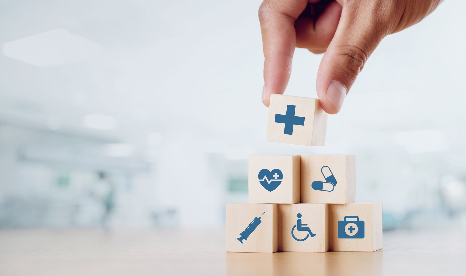 A hand is stacking wooden blocks with medical icons on them.