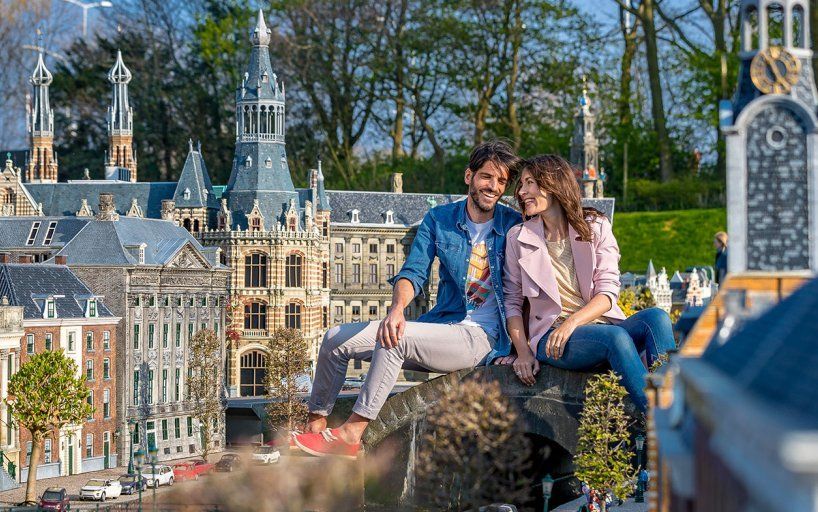 A man and a woman are sitting on a rock in front of a model city.