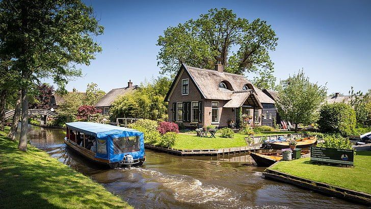 A boat is going down a river in front of a house.