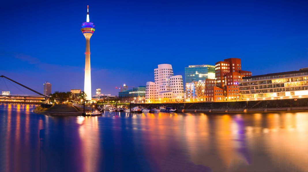 Een stadsgezicht bij nacht met een toren op de voorgrond en een watermassa op de voorgrond.