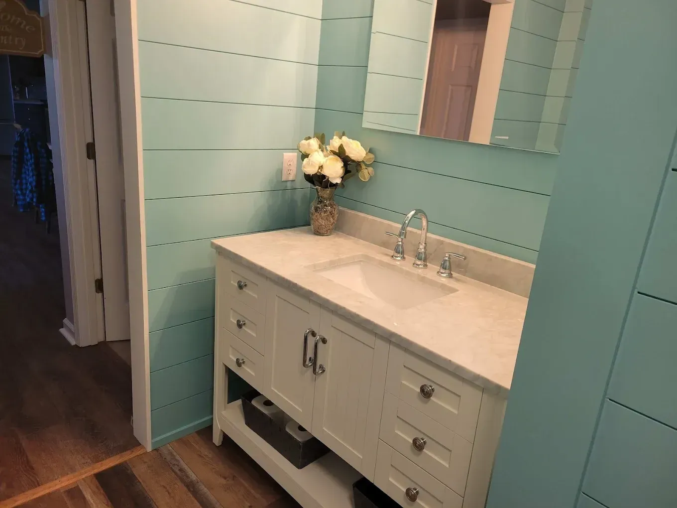 Bathroom with a white vanity, a light blue shiplap wall, and a floral arrangement.