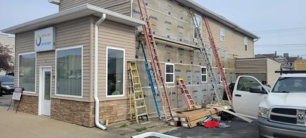 Building undergoing siding renovation, ladders propped against the exterior, work in progress.