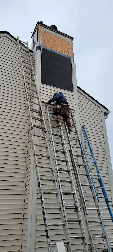 Person climbs a ladder on a house to work on the chimney.