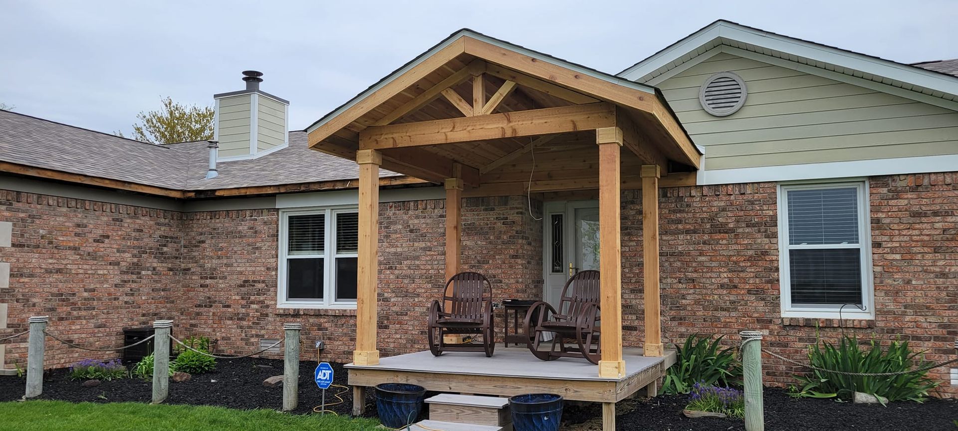 A wooden porch covers a brick house's front door; two rocking chairs sit on the porch.
