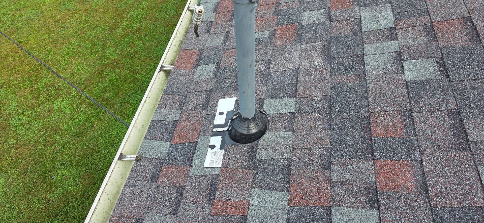 Overhead view of a roof with shingles, a vent pipe, and a green lawn.