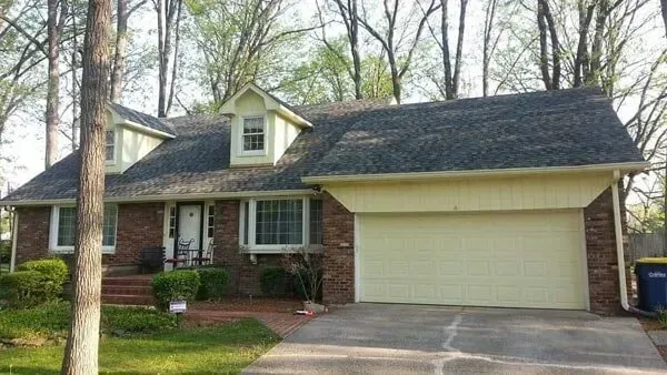 Brick house with a light yellow garage door, dormers, and a dark shingled roof.