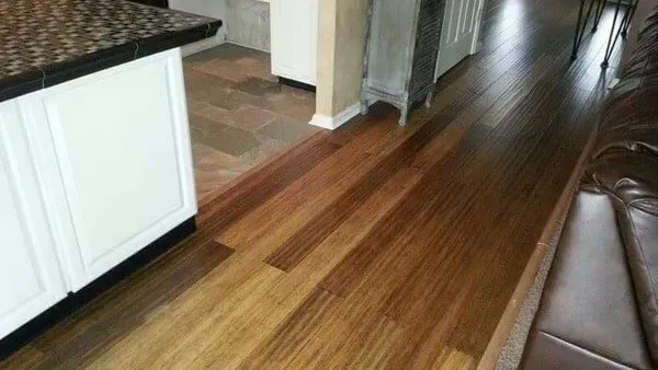 Hardwood flooring transitions to stone tile near white kitchen cabinetry.