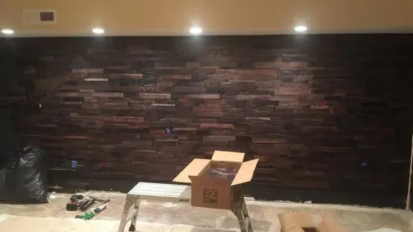 Dark wooden wall with overhead lighting, a cardboard box, and a black trash bag in a room.