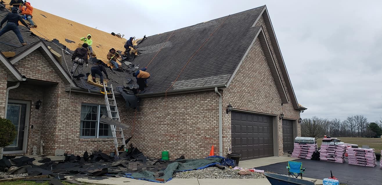 Roofers working on a residential home with exposed sheathing and a ladder. Bricks, a garage, and materials are also visible.