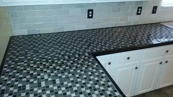 Kitchen countertop with black, white, and gray tile, white cabinets, and gray brick backsplash.