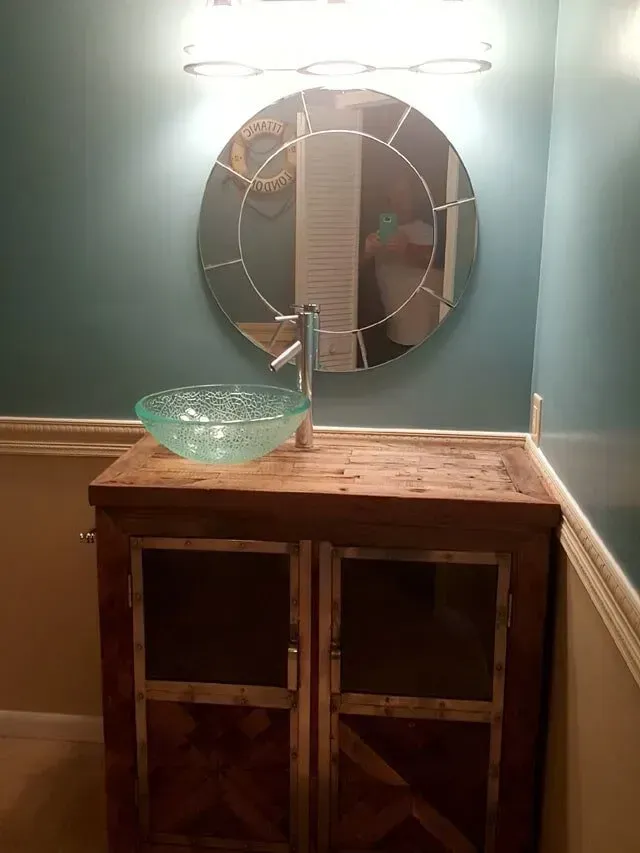 A bathroom vanity with a rustic wooden cabinet, glass vessel sink, and round mirror.