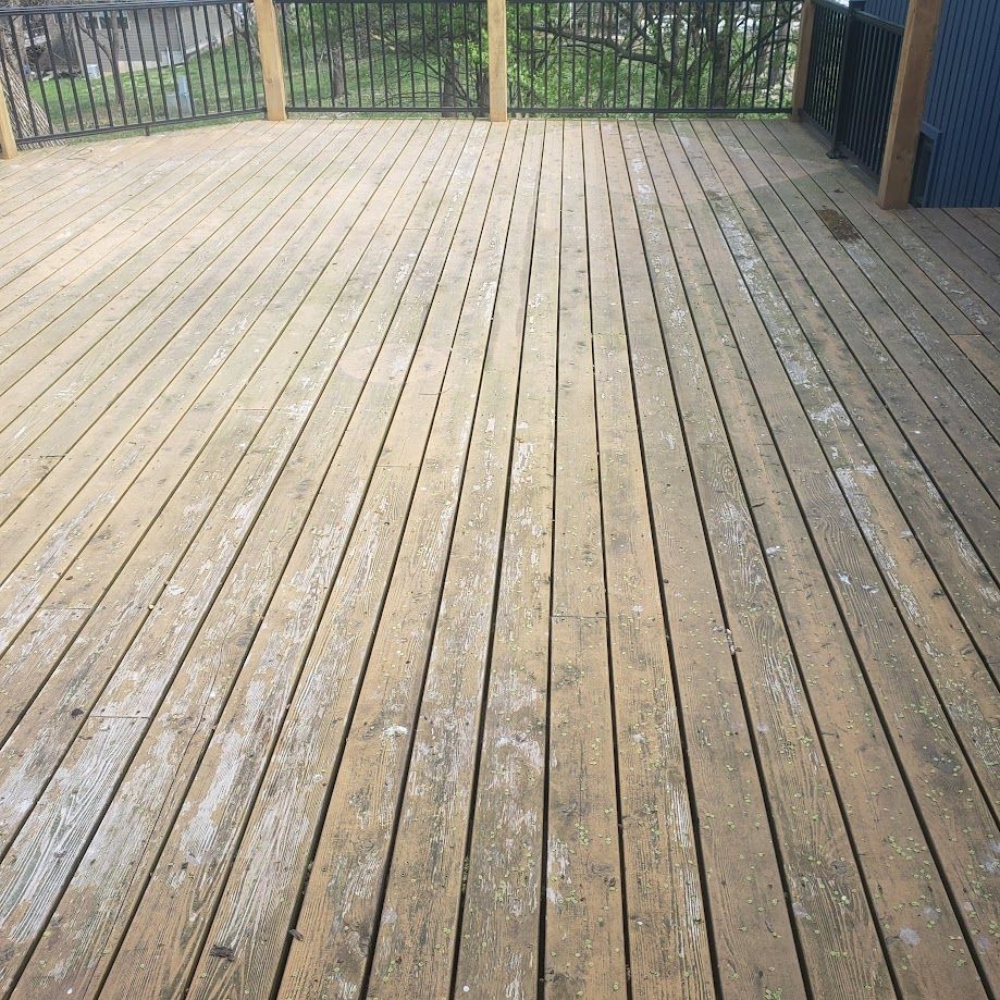 A wooden deck with a metal railing and a fence in the background.