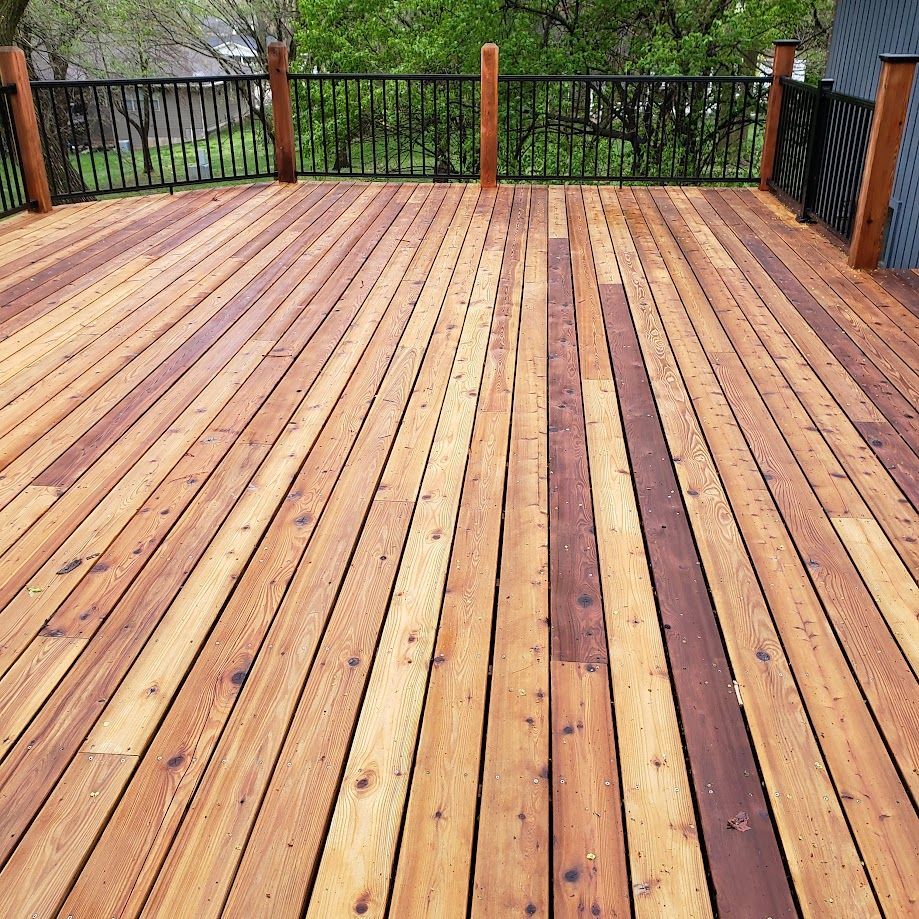 A wooden deck with a metal railing and trees in the background.