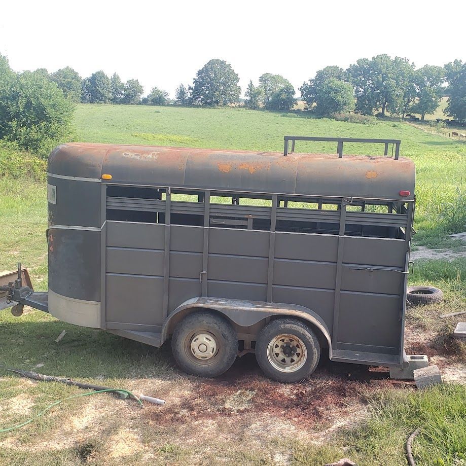 A horse trailer is parked in a grassy field.