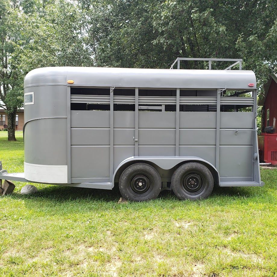 A horse trailer is parked in a grassy field.