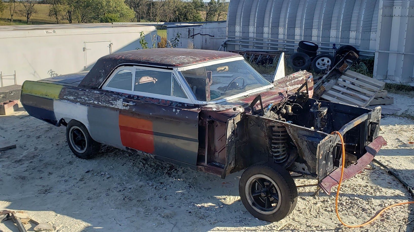 A wrecked car is sitting in the dirt in front of a building.