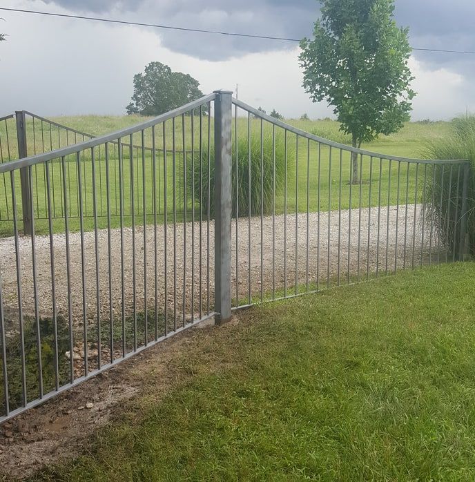 A metal fence surrounds a grassy field with trees in the background